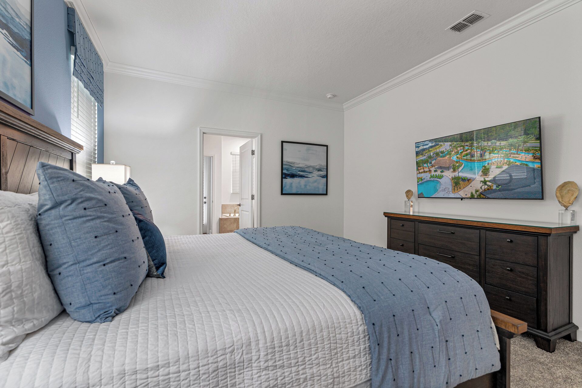 A bedroom with a bed, a dresser, a painting, and a door leading to another room.