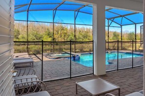 A covered outdoor area with a pool, lounge chairs, and a view of a forested area. - 8BR Villa - Game Room & Themed Rooms (Kissimmee)