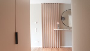 Una habitación con piso de madera, puerta corredera, espejo y una pequeña repisa con un florero.