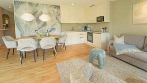 Una sala de estar moderna con sofá, una mesa de comedor con sillas, una zona de cocina con armarios y lámparas colgantes.