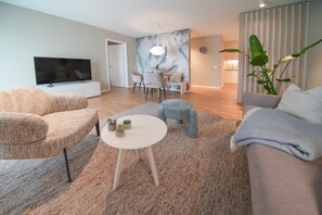 Una sala moderna con un televisor de pantalla plana, un sofá, una mesa de centro y una zona de comedor con sillas y una mesa.