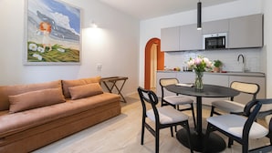 Un salon moderne avec un canapé marron, une table à manger avec des chaises et un coin cuisine équipé d’un four à micro-ondes et d’un évier.