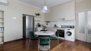 Une cuisine moderne équipée d’un réfrigérateur, d’un four à micro-ondes, d’un grille-pain et d’un lave-linge. On y trouve une table à manger avec des chaises et un luminaire suspendu.