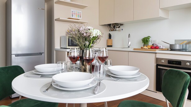 Une cuisine moderne avec une table à manger dressée pour quatre personnes, agrémentée d’assiettes blanches, de verres et de couverts.