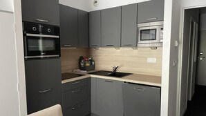 A compact kitchen with grey cabinets, a black oven, a microwave, and a sink. - 150m from ski slopes, 1st floor, swimming pool, tv, ski locker, 30m², Gourette (Eaux-Bonnes)