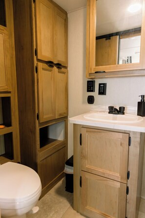 Ein Badezimmer mit Holzschränken, einem weißen Waschbecken und einer Toilette.