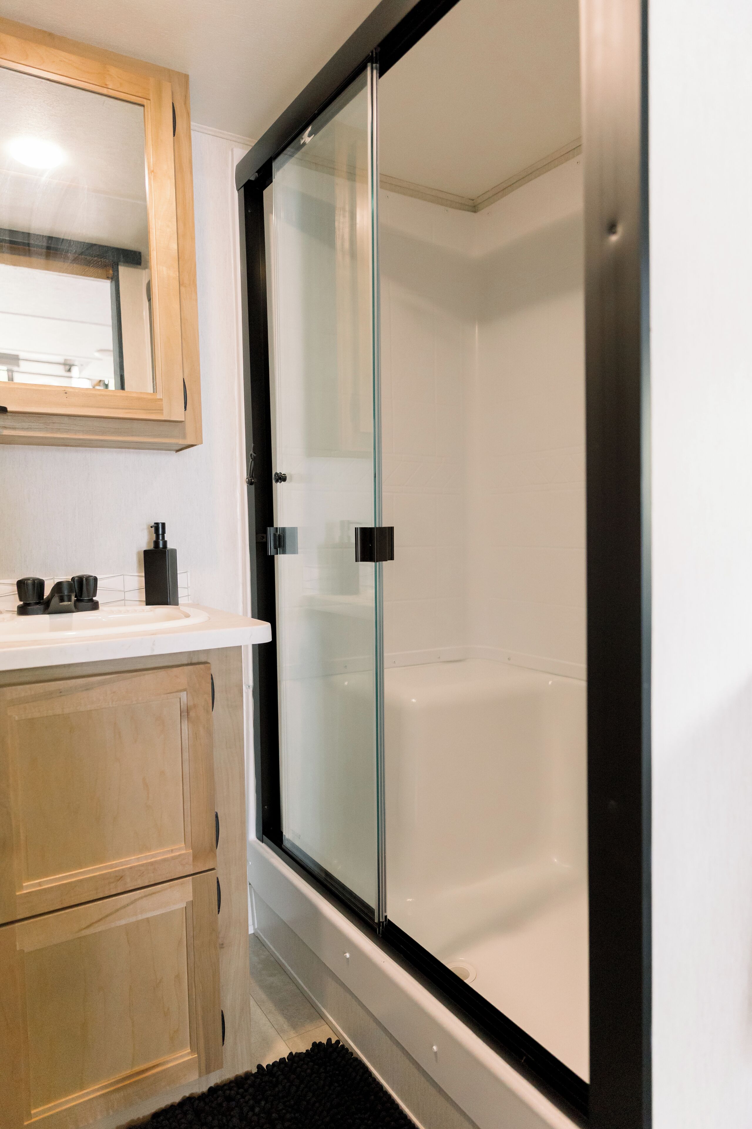 Un bagno con cabina doccia in vetro, mobile bagno in legno e specchio sopra il lavandino.