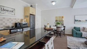A modern kitchen with a central island, wooden cabinets, and a dining area with a green sofa and a table.