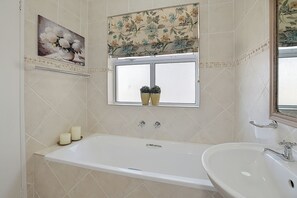 Une salle de bain avec une baignoire, un lavabo, une fenêtre ornée de plantes en pot et un rideau de douche à motifs floraux.