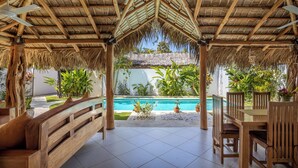 Un espace extérieur abrité comprenant une piscine, des meubles en bois et des plantes tropicales.
