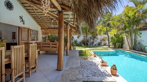 Un espace extérieur abrité comprenant une piscine, des meubles en bois et des plantes en pot.