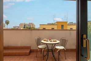 Ein Balkon mit einem Tisch für zwei Personen, Stühlen und Blick auf Gebäude im Hintergrund.