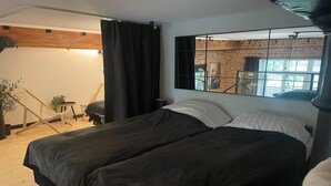 A bedroom with a large bed, a window with a view of a brick wall, and a chair in the corner. - A Comfortable Apartment in the Heart of the City (Łódź)