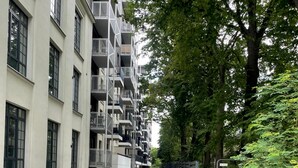 Um edifício moderno de vários andares com varandas, um passeio pavimentado e uma cerca.