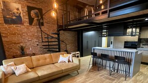 A modern interior with a brick wall, a sofa, a dining area with bar stools, and a staircase. - A Comfortable Apartment in the Heart of the City (Łódź)