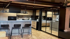 A modern kitchen with a central island, bar stools, and a view into another room through a glass partition. - A Comfortable Apartment in the Heart of the City (Łódź)