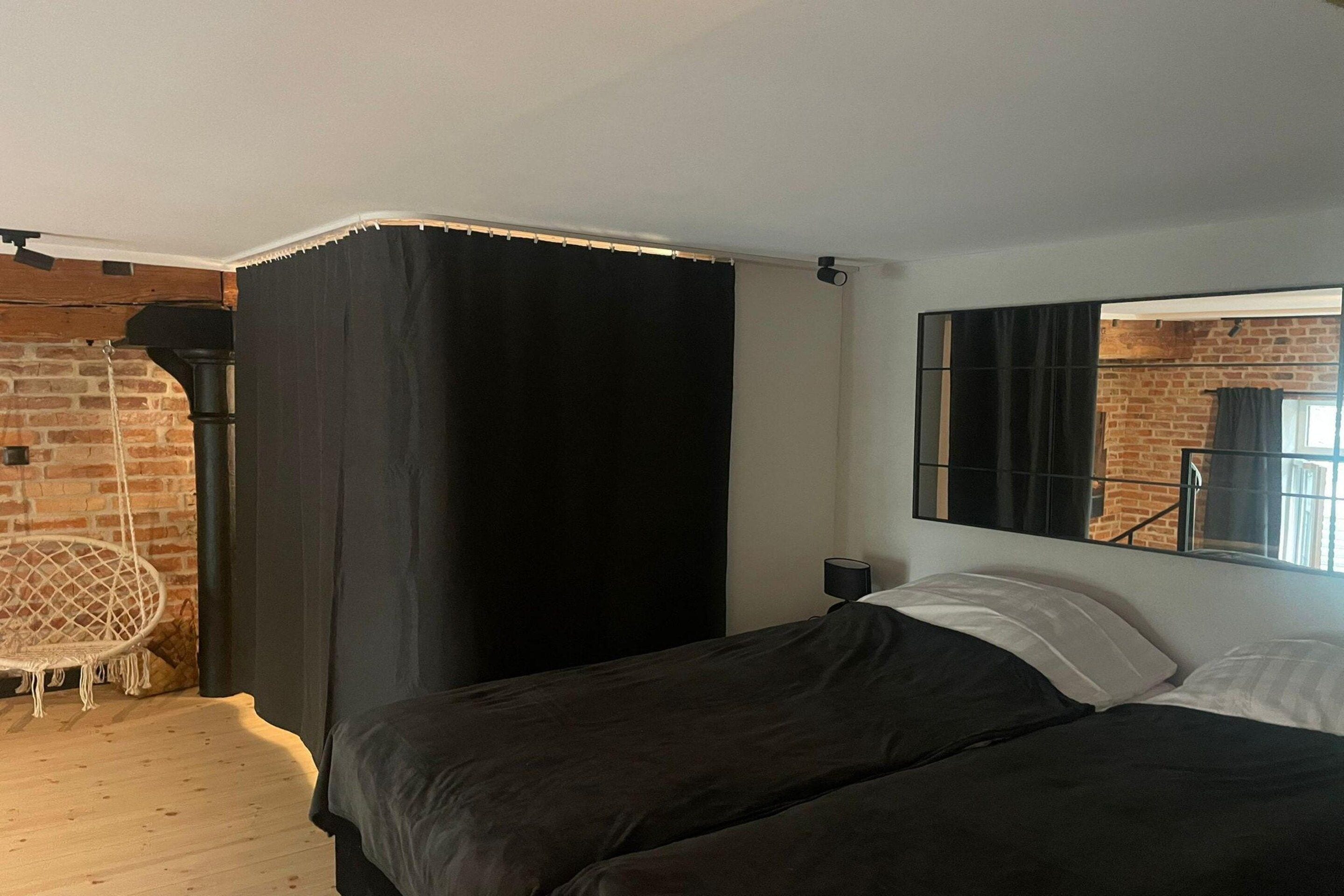 Quarto com cama, uma cadeira e janela com vista para uma parede de tijolos.