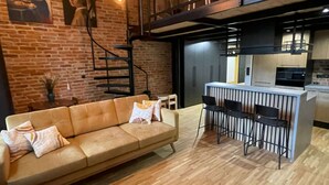 Uma sala de estar moderna com sofá, área de refeições com cadeiras, cozinha e escada.