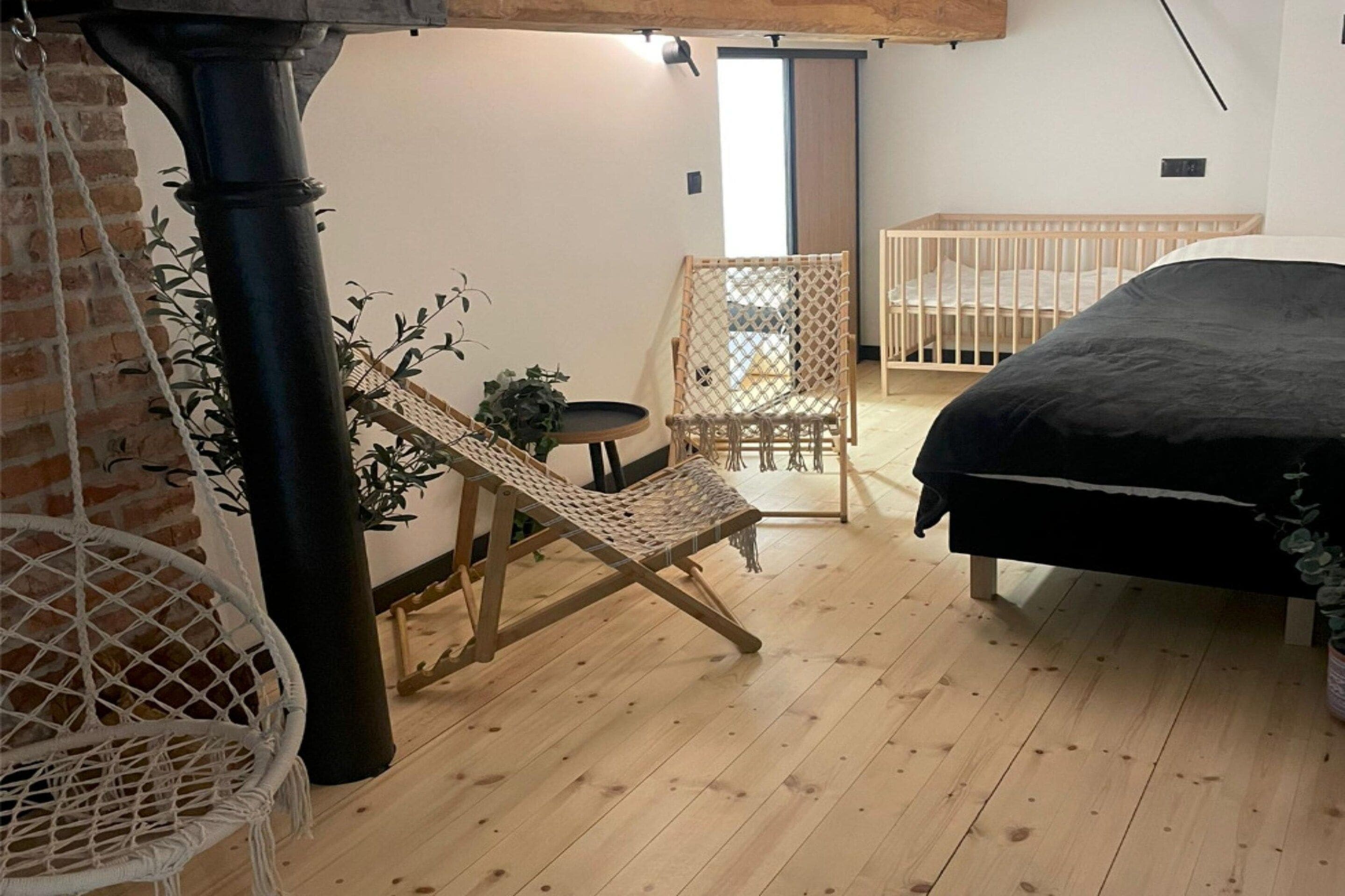Ein Zimmer mit einem Bett, einem Sessel, einem Babybett und einem Hängesessel.