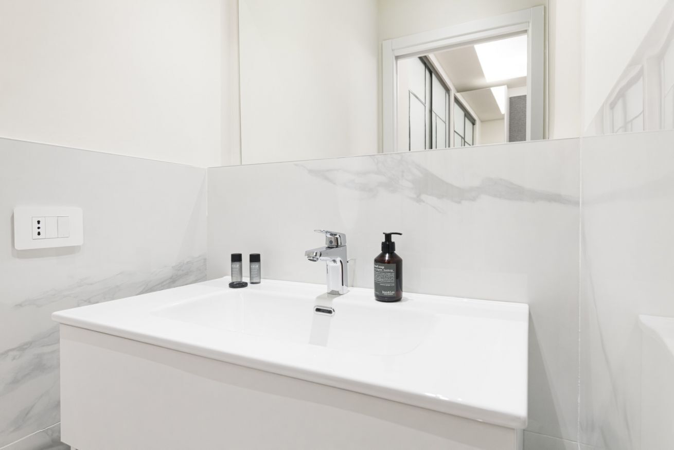 A modern bathroom with a white sink, a mirror, and a bottle of lotion.