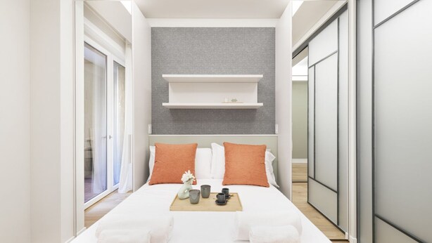 A modern hotel room with a large bed, two pillows, a tray with cups and a vase, and a view of the outside.