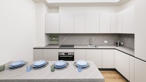 A modern kitchen with white cabinets, a marble countertop, and a built-in oven.