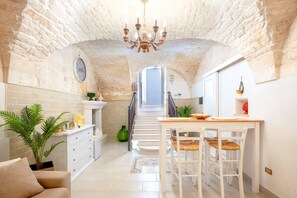 Une cuisine spacieuse avec un escalier menant à un balcon, un coin repas avec des meubles blancs et une grande plante verte.