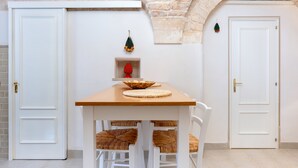 A room with a wooden table, white chairs, a white door, and a stone wall.