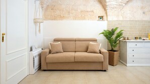 A beige sofa with cushions, a white door, a stone wall, a potted plant, and a white cabinet.