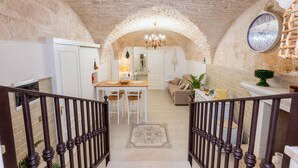 A stone-walled interior with a dining area, staircase, and a clock on the wall.