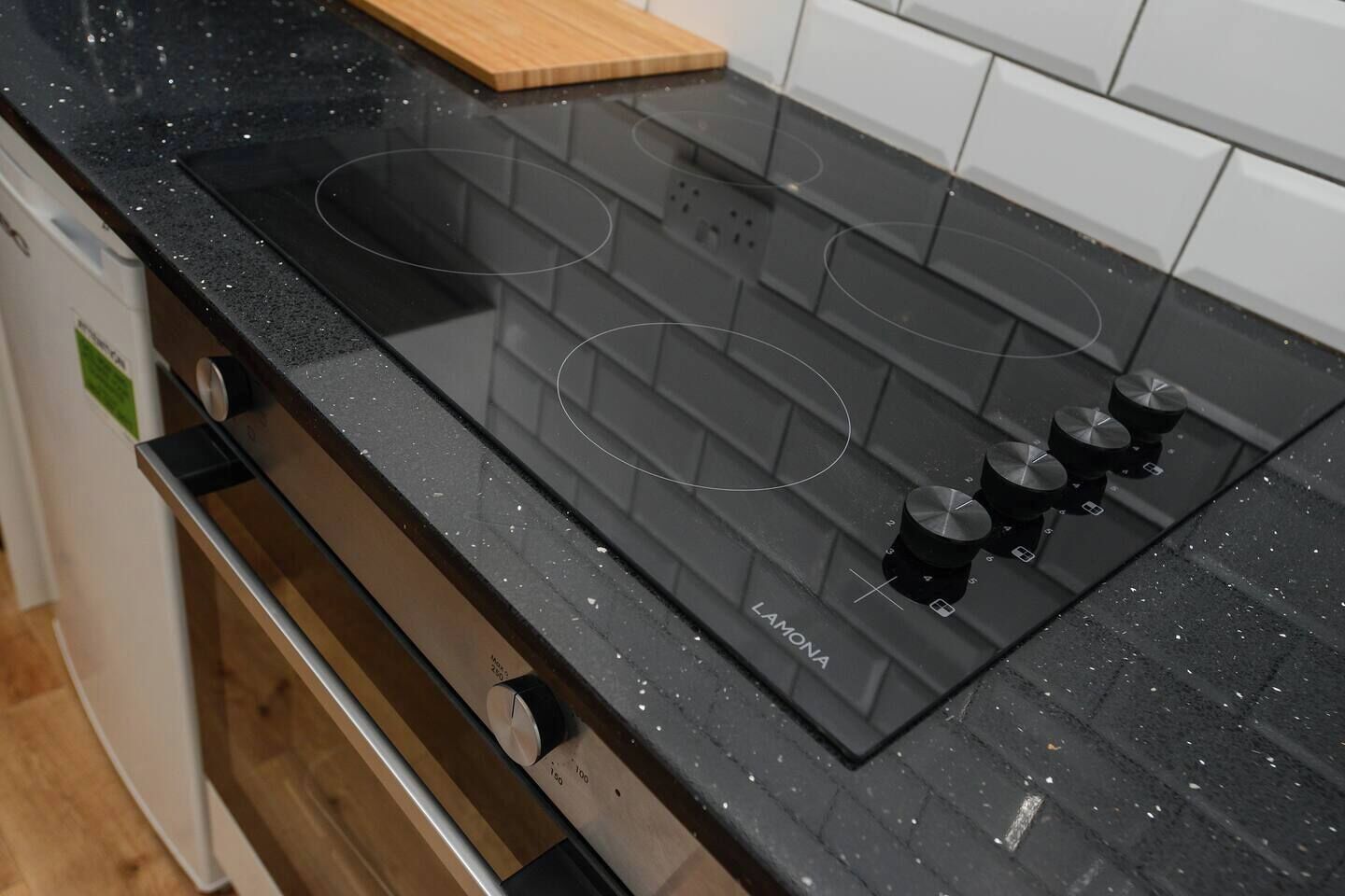 Una cocina con una placa de inducción negra, cuatro perillas y una tabla de cortar de madera en la encimera.