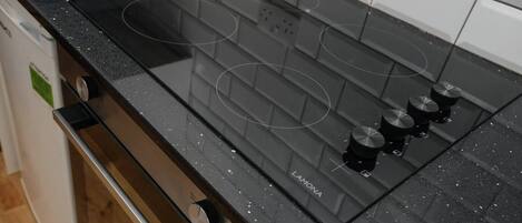 Una cocina con una placa de inducción negra, cuatro perillas y una tabla de cortar de madera en la encimera.