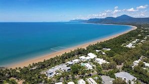 An aerial view of a coastal area with a beach, houses, and a mountain in the background.