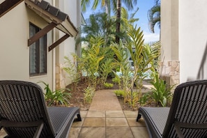 A patio with two wicker chairs, a pathway, and tropical plants.