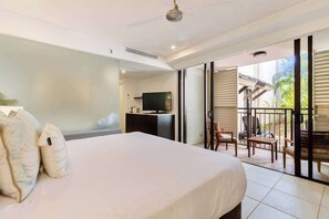 A bedroom with a bed, a TV, and a balcony with chairs.