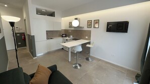 A modern kitchen with white cabinets, a built-in oven, and a dining area with two white bar stools.