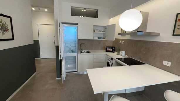 A modern kitchen with a built-in dishwasher, a sink, a stove, and a dining area with a table and chairs.
