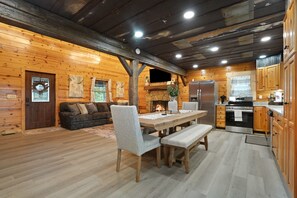 A log cabin interior with a dining area, kitchen, and living room.