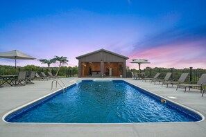 A rectangular swimming pool with a covered seating area in the center, surrounded by lounge chairs and umbrellas.