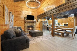 A cozy log cabin interior with a fireplace, a sofa, a dining table, and a kitchen area. - The View at Grizzly Mountain | Hocking Hills, Pool (Creola)