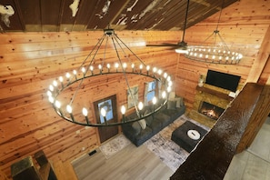 A log cabin interior with a circular chandelier, a fireplace, a sofa, and a television. - The View at Grizzly Mountain | Hocking Hills, Pool (Creola)
