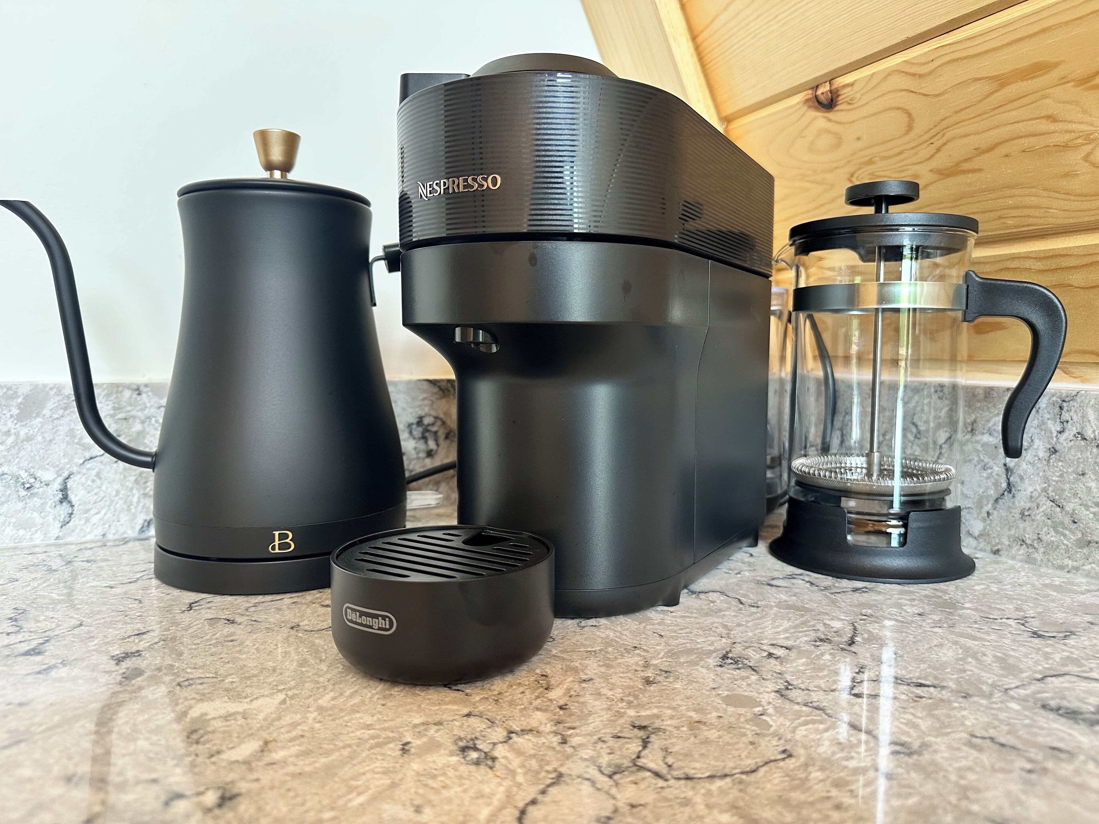 Une machine à café, une bouilloire et une cafetière à piston sur un plan de travail en marbre.