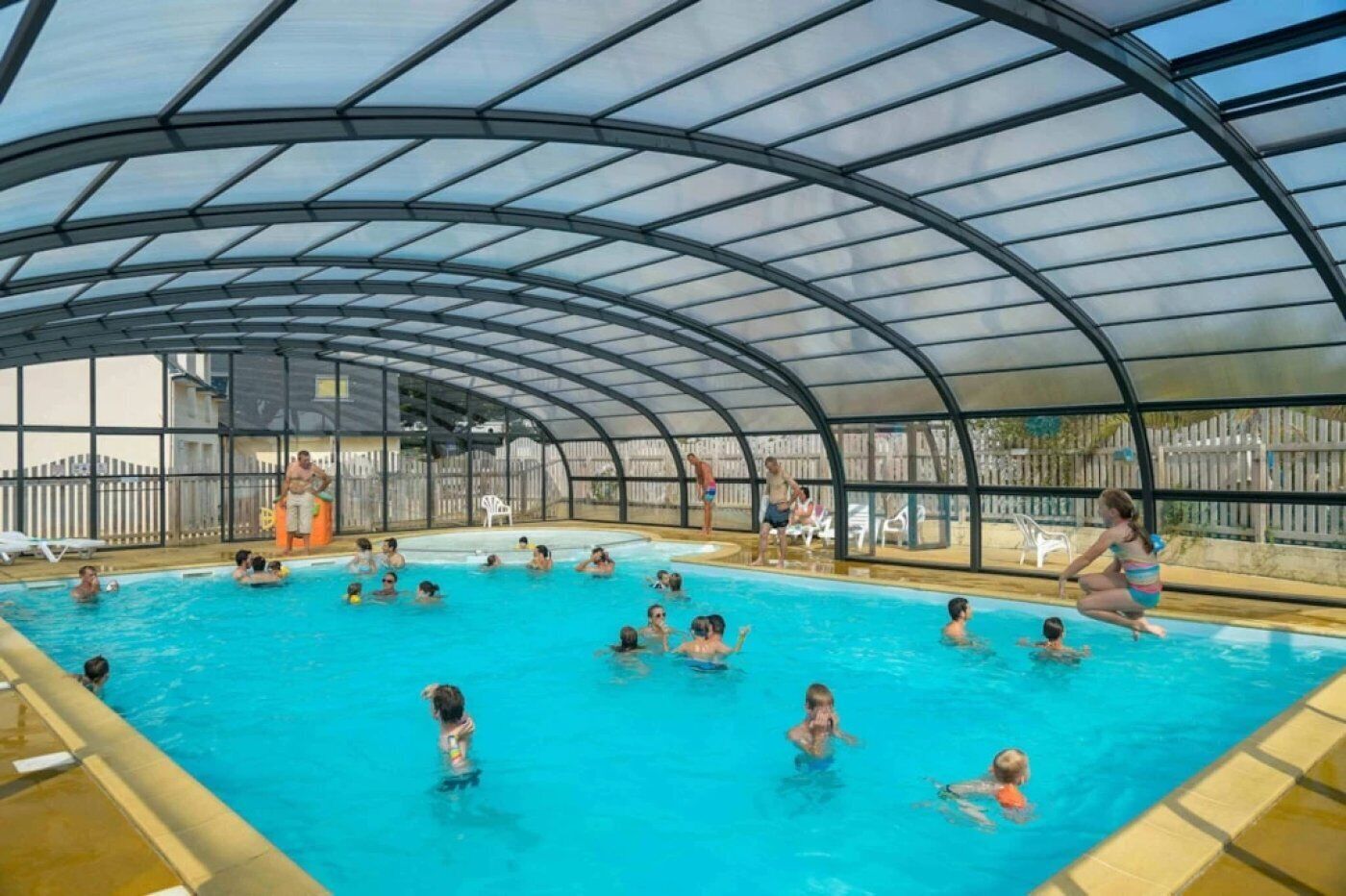 Una piscina interior con techo de vidrio curvo, rodeada por una valla.