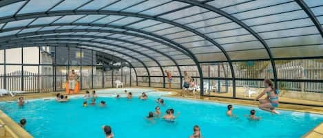 Una piscina interior con techo de vidrio curvo, rodeada por una valla.