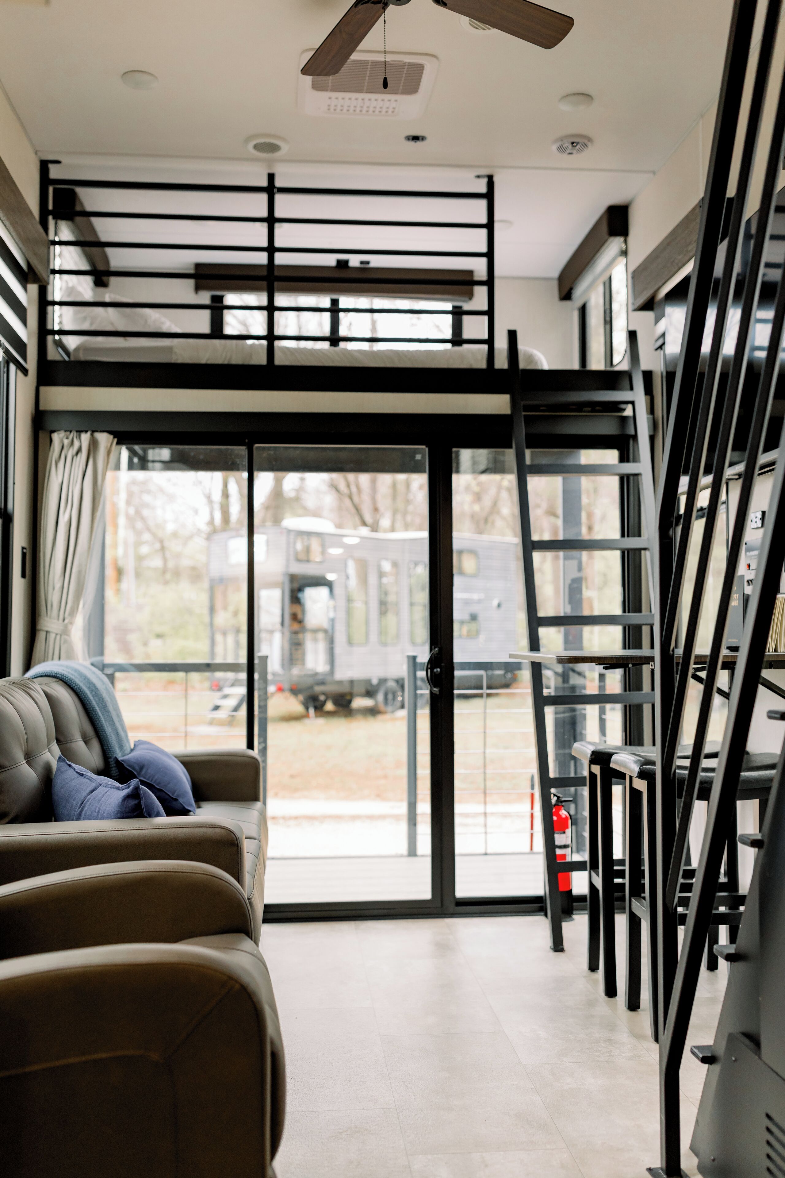 Un interior de autocaravana moderna con una litera, una zona de estar con sofá y una puerta corredera que da a un espacio exterior.