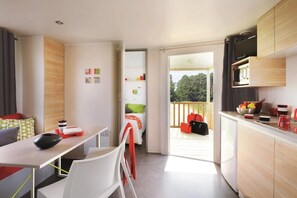 A compact, modern room with a kitchenette, a dining area, and a balcony with luggage.