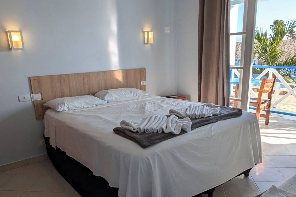 Ein Hotelzimmer mit Bett, Nachttisch, Wandklimaanlage und einem fenster mit Vorhängen.