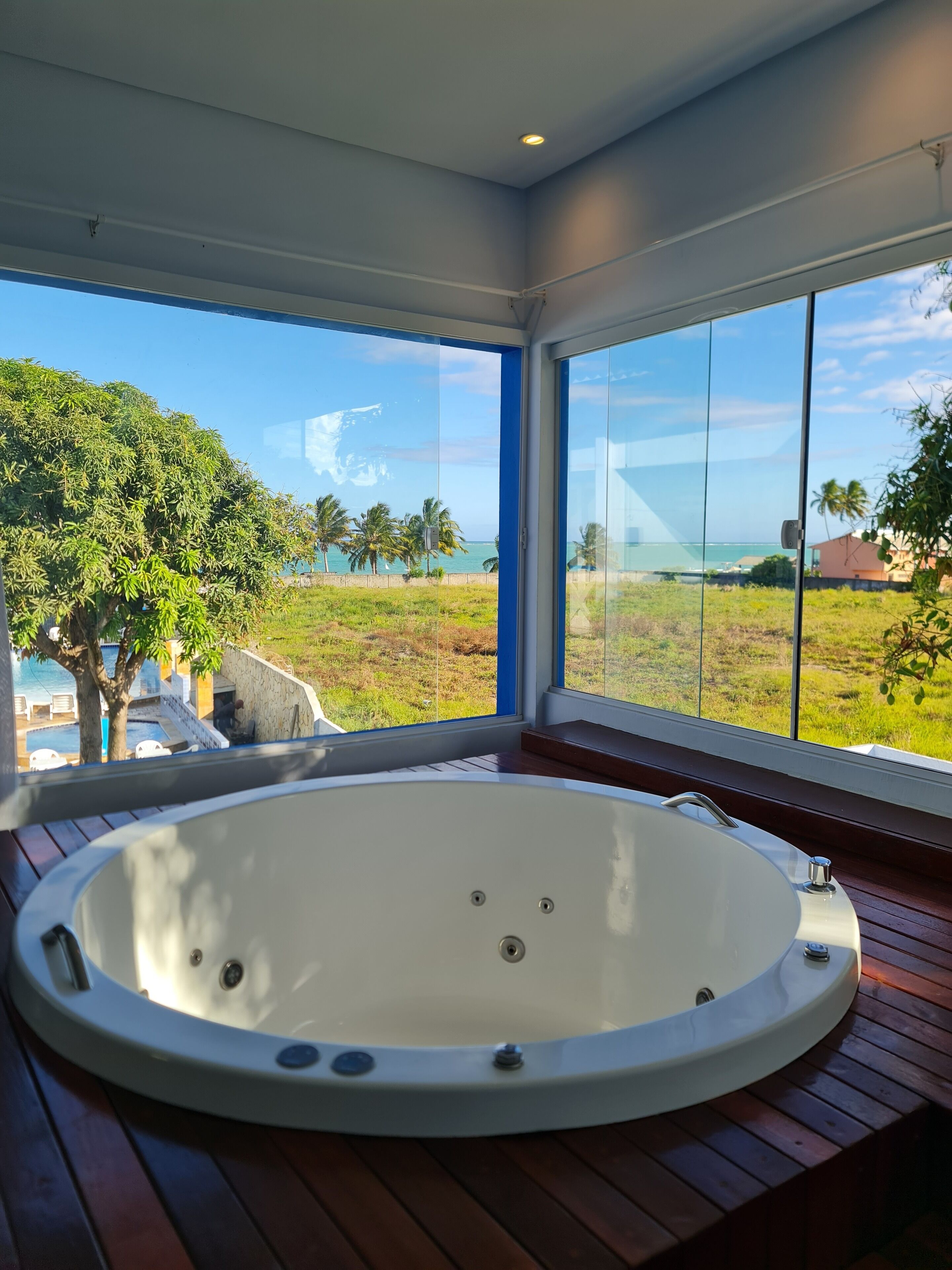 A modern bathroom with a large bathtub, large windows, and a view of a pool and greenery.