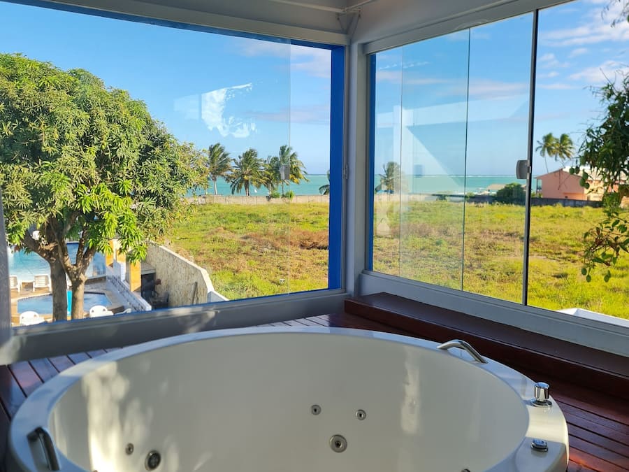 Un baño moderno con una bañera amplia, ventanas grandes y vistas a una piscina y zonas verdes.