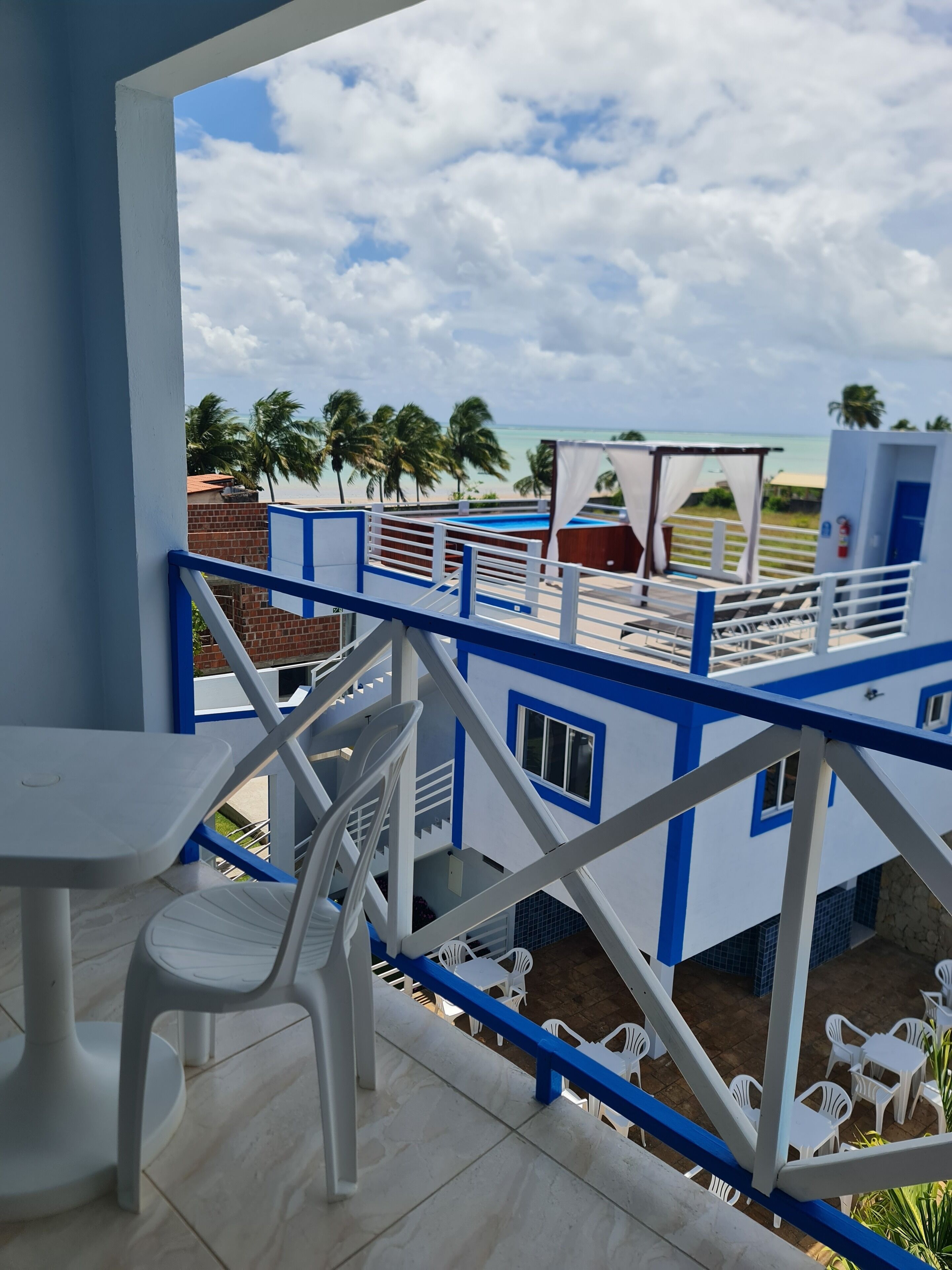 Un balcón con vista a la playa, palmeras y una piscina.